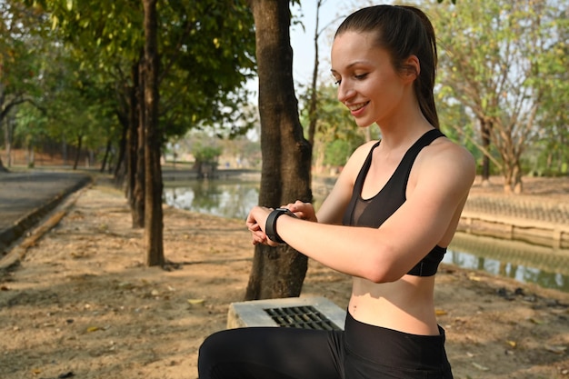 Mooie sportieve vrouw die rust na een trainingssessie en fitnessresultaten of hartslag op smartwatch controleert