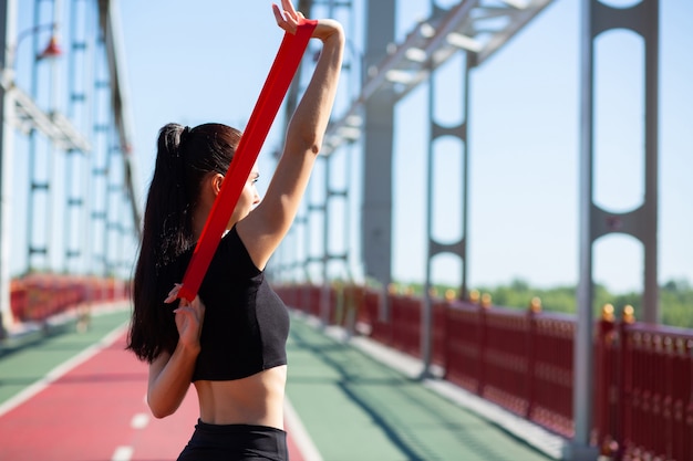 Mooie sportieve vrouw doet training met rubberen weerstandsband op een brug. Ruimte voor tekst