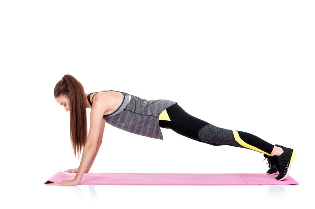 mooie sportieve vrouw in sportkleding doet oefeningen op fitness Mat geïsoleerd op een witte achtergrond. plank