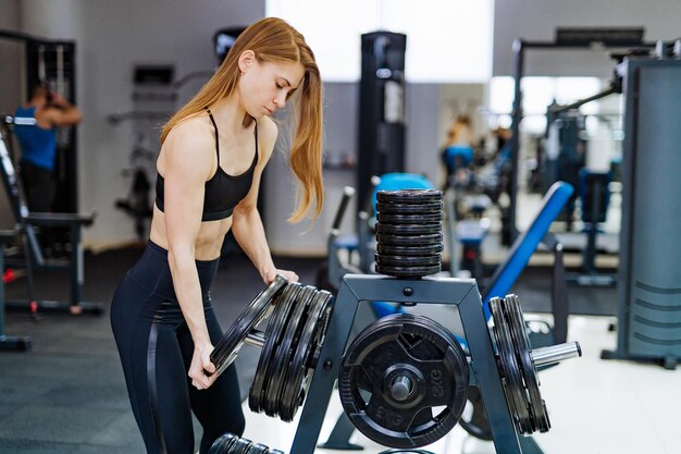 Mooie sterke jonge sportvrouw zet barbell-schijf in sportschool Actieve fitnessvrouw met halterplaten in sportschool