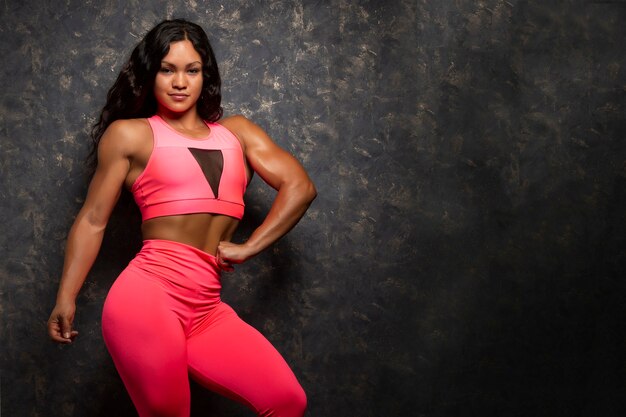 Mooie sterke jonge vrouwelijke bodybuilder atleet poseren in fuchsia sportkleding