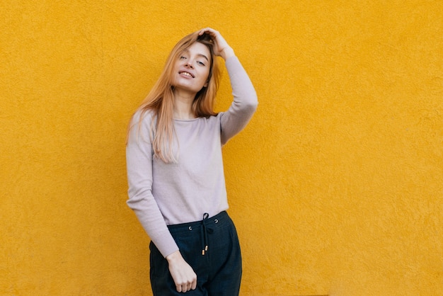 Mooie stijlvolle jonge blonde meisje poseren tegen een gele muur achtergrond, glimlachend