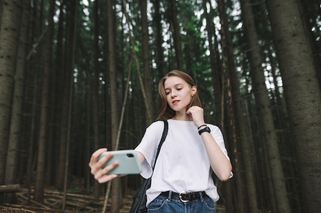 Mooie stijlvolle toeristische vrouw met behulp van haar telefooncamera om een selfie te maken in het sparrenbos van de bergen