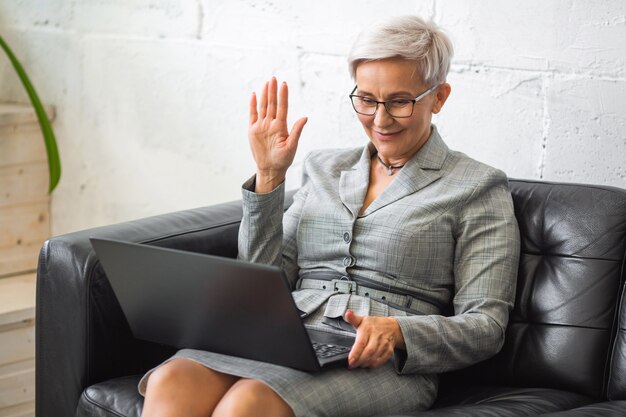 mooie stijlvolle volwassen vrouw in pak werken met laptop op zwarte bank