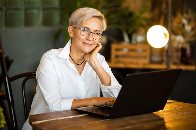 Mooie stijlvolle vrouw in glazen verouderd aan tafel met een laptop