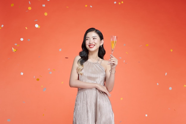 Mooie stijlvolle vrouw in vakantie-outfit met champagne tegen de rode achtergrond van confetti