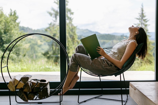 Foto mooie stijlvolle vrouw ontspannen met boek in modern chalet met uitzicht op bergen vrije tijd