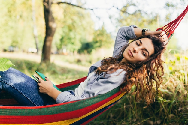 Mooie studente die in het park rusten dat in een hangmat ligt en een boek leest