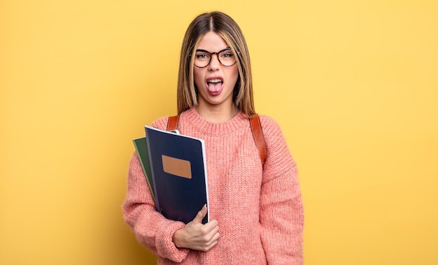 Mooie studentenvrouw die walgt en geïrriteerd voelt en tong uitsteekt. boeken en rugzak