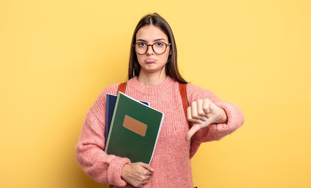 Mooie studentenvrouw die zich boos voelt en duimen naar beneden laat zien