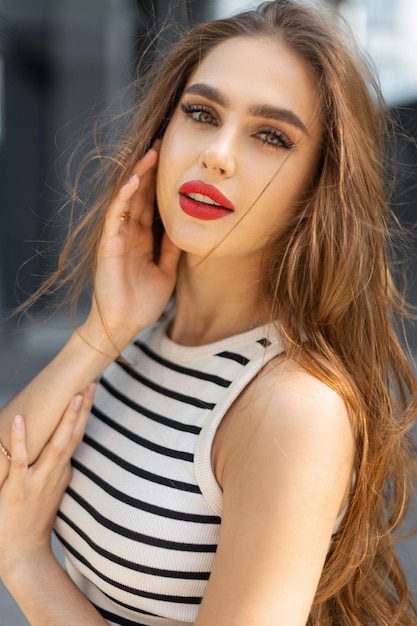 Foto mooie tedere jonge frisse vrouw met rode lippen in stijlvolle zomerkleren lopend en kijkend naar de camera op straat
