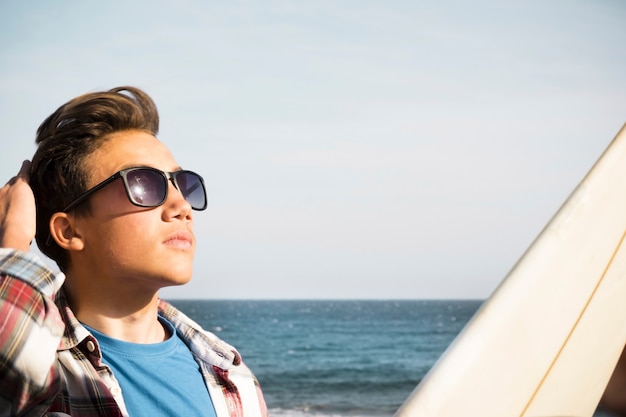 Mooie tiener met zonnebril die naar de lucht kijkt - surferjongen met een surftafel op auto - vakantie- en reislevensstijl