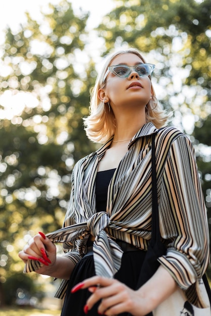 Mooie tiener vrouw met zonnebril in fashion vintage shirt en zwarte jurk wandelingen in het park