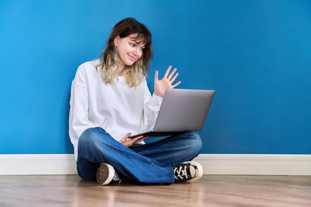 Mooie tiener vrouwelijke zittend op de vloer met laptop op blauwe achtergrond