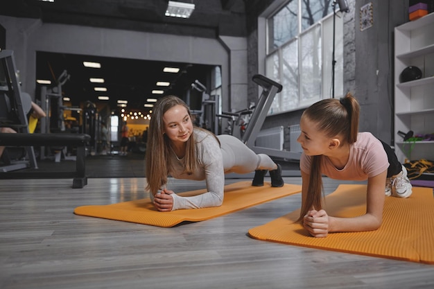 Mooie tienermeisje lacht naar haar personal trainer terwijl ze samen plankoefeningen doet in de sportschool kopieerruimte