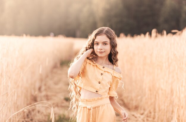 Mooie tienermeisje met lang haar wandelen door een tarweveld op een zonnige dag. Buiten portret. Schoolmeisje ontspannen