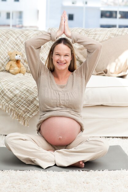 Mooie toekomstige moeder die yogapositie op de vloer doet