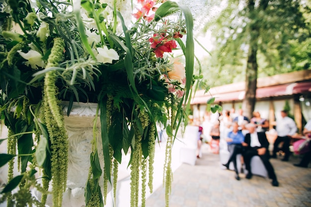 Foto mooie trouwfotozone in het park in de schaduw, een wit scherm, een voetstuk met bloemen en decor.