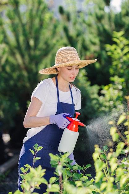 Mooie tuinman vrouw in stro hoed hagelslag planten uit een tuin sproeier.