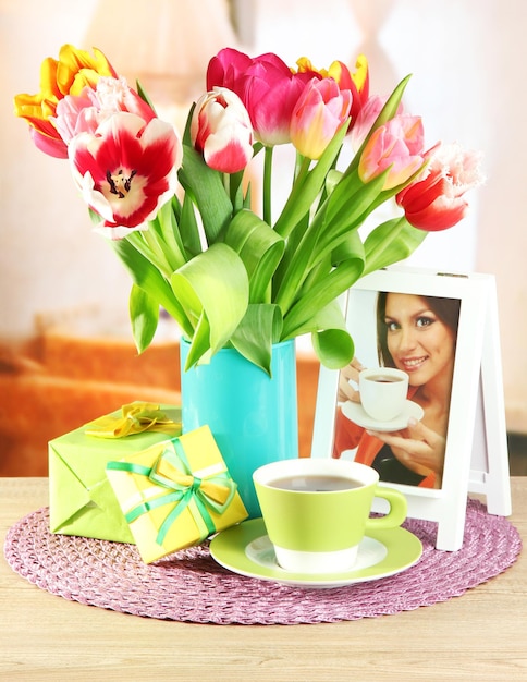 Mooie tulpen in emmer met cadeautjes en kopje thee op tafel op kamer