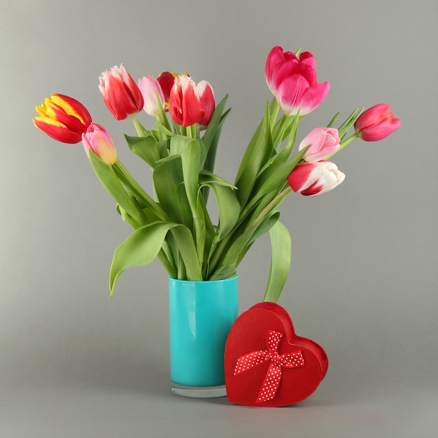 Mooie tulpen in emmer met geschenken op grijze ruimte