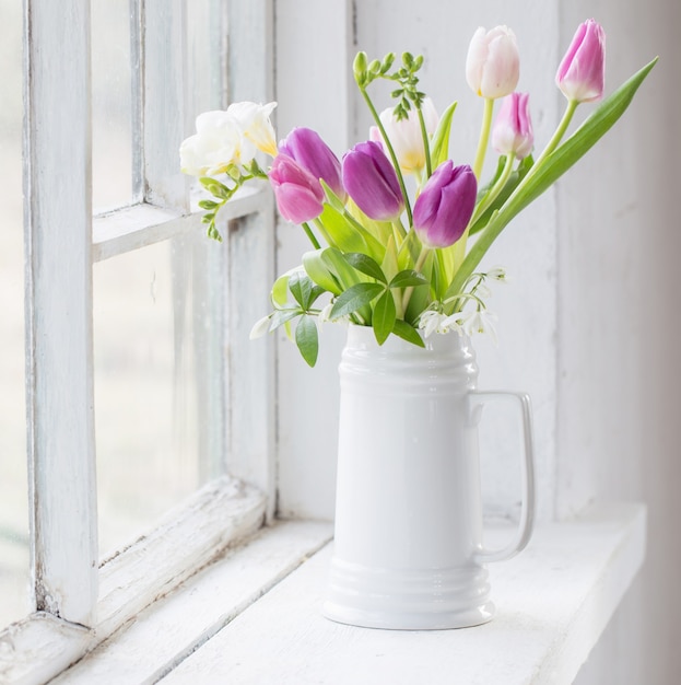 Mooie tulpen in kruik op oude witte vensterbank