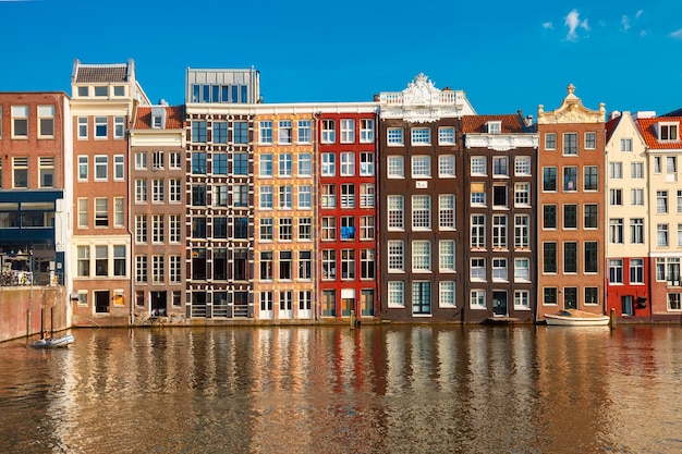 Mooie typisch Nederlandse dansende huizen aan het Amsterdamse kanaal Damrak in zonnige dag, Holland, Nederland.