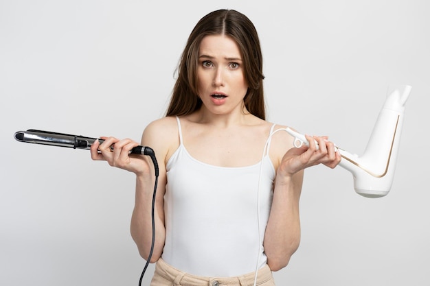 Mooie verbaasde vrouw met haarregelaar en haardroger geïsoleerd op witte achtergrond