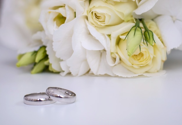 Mooie verlovingsringen en bruidsboeket van witte bloemen op een witte ondergrond