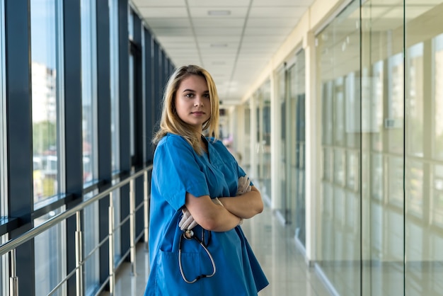 Mooie verpleegster in blauw uniform met stetoscoop binnenshuis in moderne kliniek. Gezondheidszorgmedewerker in het ziekenhuis die op het diagnostiseren van patiënten wacht