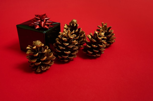 Mooie vijf dennenappels versierd met gouden verf en luxe kerstcadeau in glanzend groen inpakpapier met glitter rode strik geïsoleerd over gekleurde rode achtergrond met kopie ruimte voor reclame