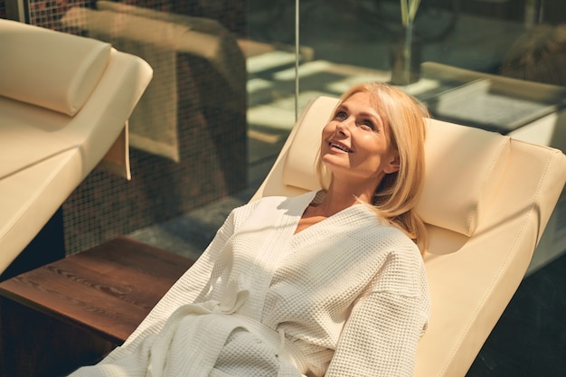 mooie volwassen dame liggend op chaise longue in badjas in het kuuroordhotel in de zondag