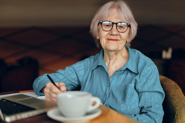 Mooie volwassen senior vrouw zitten in een café met een kopje koffie en een laptop Freelancer werkt ongewijzigd