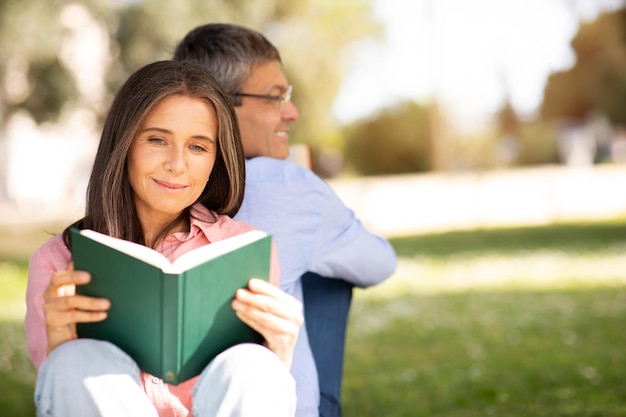 Mooie volwassen vrouw die een boek leest terwijl ze met haar man in het park ontspant.