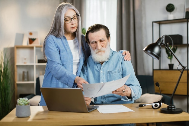 Mooie volwassen vrouw en bebaarde man in casual outfit met behulp van laptop tijdens het samenwerken