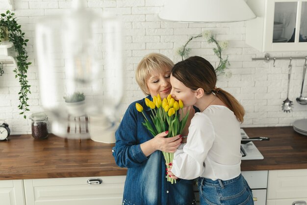 Mooie volwassen vrouw geeft bloemen aan haar volwassen moeder Vrouwendag