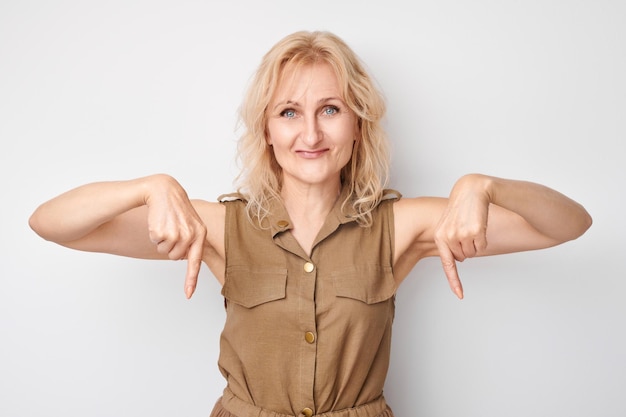 Foto mooie volwassen vrouw van 50 jaar die met de vinger naar beneden wijst en een lege ruimte voor product of tekst toont die isoleerd is op een witte achtergrond in de studio