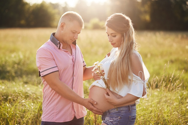 mooie vriendelijke familie anticiperen op een baby, buiten staan, een wandeling maken over het zomerveld