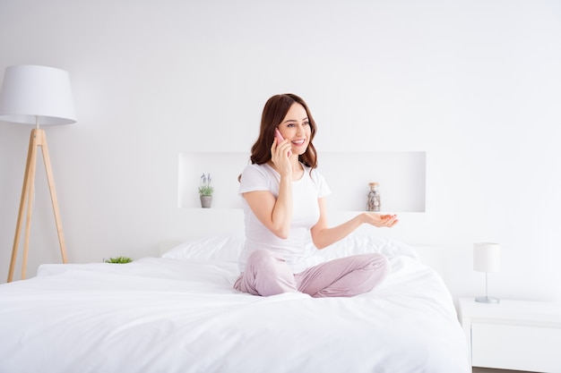 mooie vrij vriendelijke meisje zittend in bed praten over de telefoon