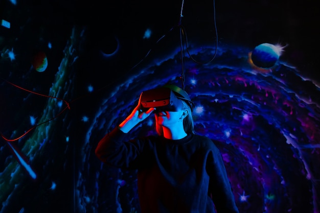 Mooie vrolijke gelukkig meisje in virtual reality-bril met blauwe en rode lichten in de speelkamer