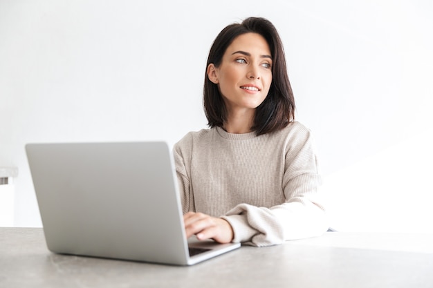 mooie vrouw 30s bezig met laptop, zittend over witte muur in lichte kamer