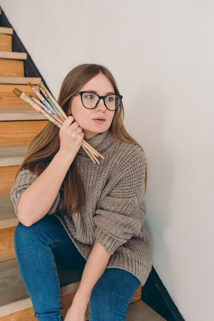 mooie vrouw artiest in bril en vrijetijdskleding zittend op trappen met borstels