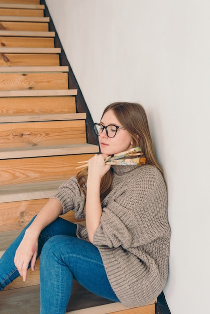 mooie vrouw artiest in bril en vrijetijdskleding zittend op trappen met borstels