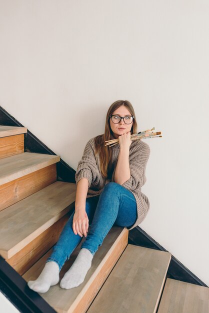 mooie vrouw artiest in bril en vrijetijdskleding zittend op trappen met borstels