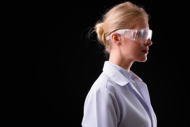 mooie vrouw arts met blond haar als wetenschapper beschermende bril tegen zwarte muur