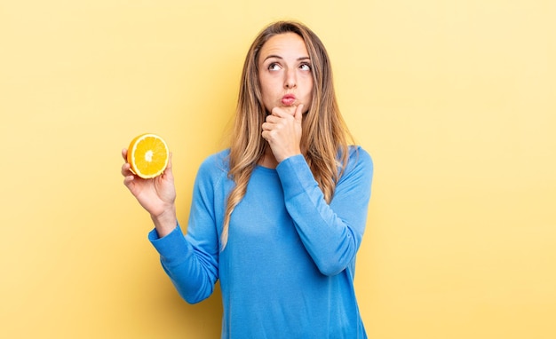 Mooie vrouw denkt, voelt zich twijfelachtig en verward terwijl ze half oranje vasthoudt