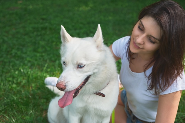 Mooie vrouw die aan haar schattige witte hond met blauwe ogen kijkt