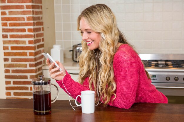 Mooie vrouw die aan muziek luistert en koffie in de keuken heeft