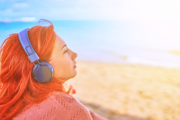 Mooie vrouw die aan muziek op het strand luistert.