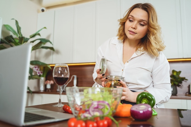 Mooie vrouw die aan tafel zit en naar het scherm van haar laptop kijkt